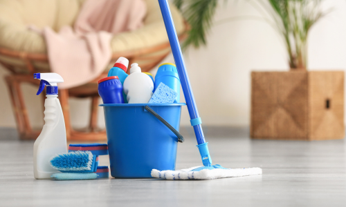 A bucket full of cleaning supplies on a kitchen floor next to a mop.